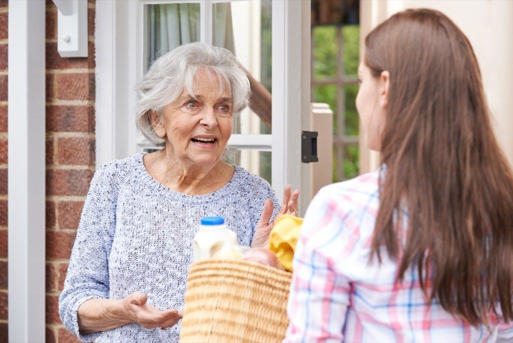 Mujer entregando comestibles a su anciano vecino