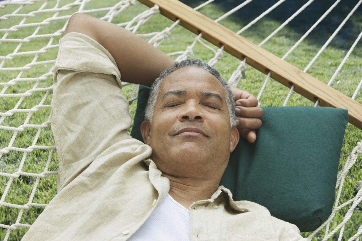 Vecāks melnādainais vīrietis guļ uz šūpuļtīklu