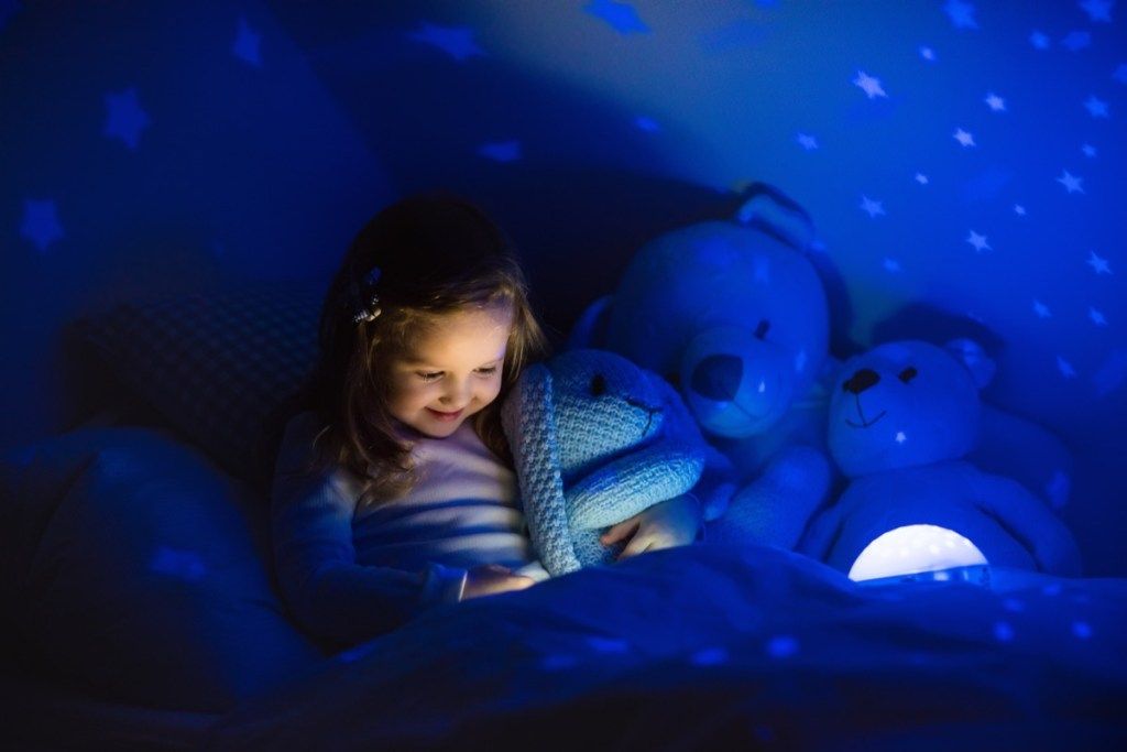 cô gái nhỏ sử dụng đèn ngủ trên giường