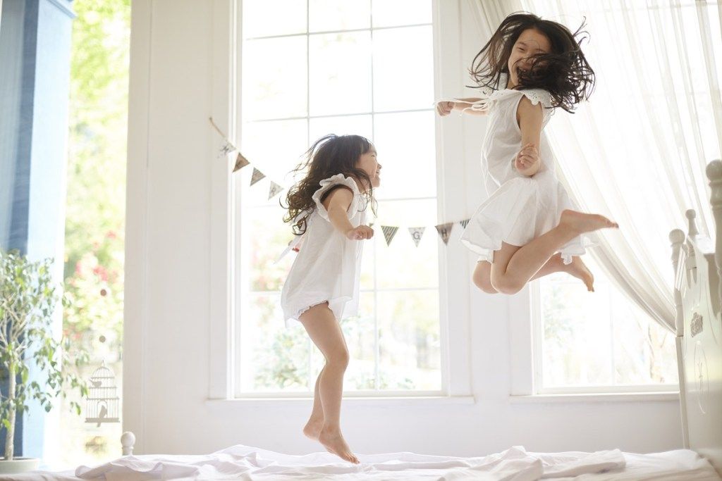 zwei junge asiatische Mädchen, die auf Bett springen