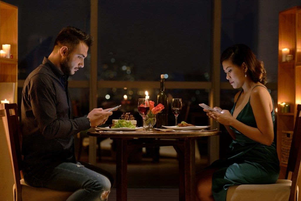 Người đàn ông da trắng và người phụ nữ châu Á nói chuyện điện thoại trong bữa tối