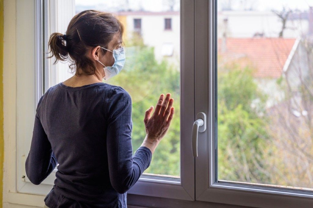 kvinne med ansiktsmaske som ser ut av vinduet hennes