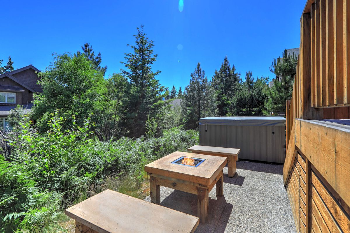 Небольшой, но открытый для зелени задний двор со столом для костра, гидромассажной ванной и деревянной террасой.