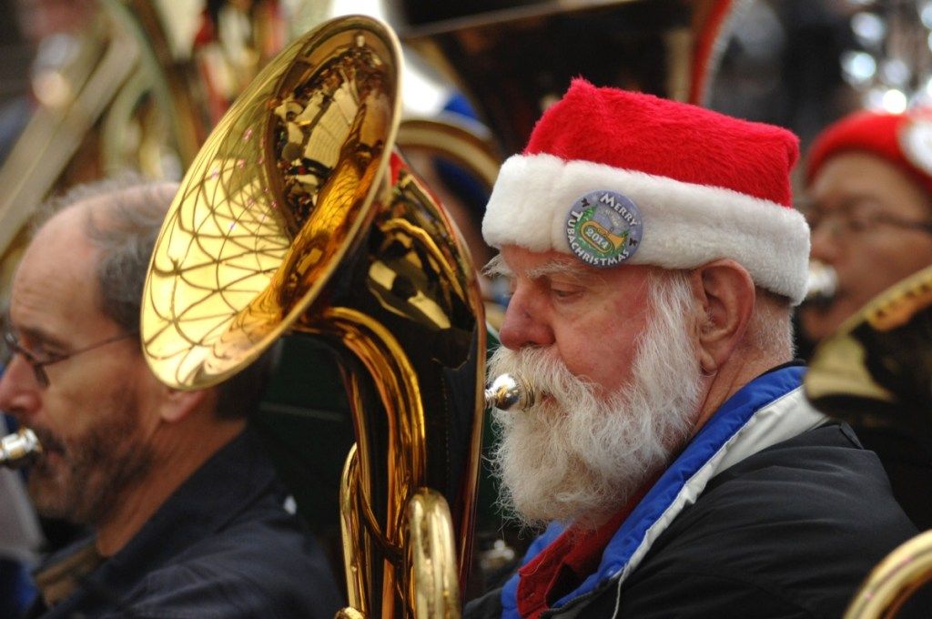 Старши мъж в шапка на Дядо Коледа свири на туба в група