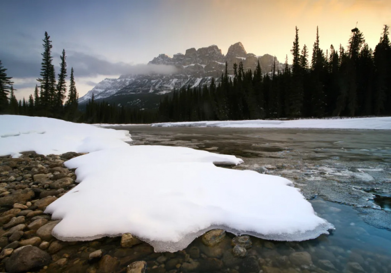   Топящ се сняг на речен бряг с канадските Скалисти планини на заден план