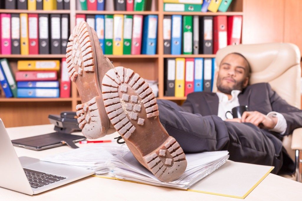 איש במשרד משועמם כשרגליו מושטות וקורא שפת גוף