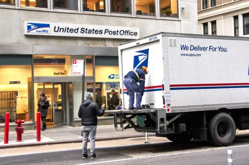   นิวยอร์ก สหรัฐอเมริกา 14 ธันวาคม 2018: บุรุษไปรษณีย์ USPS บนรถบรรทุกส่งของทางไปรษณีย์ในนิวยอร์ก USPS เป็นหน่วยงานอิสระของรัฐบาลกลางสหรัฐที่รับผิดชอบในการให้บริการไปรษณีย์ในสหรัฐอเมริกา