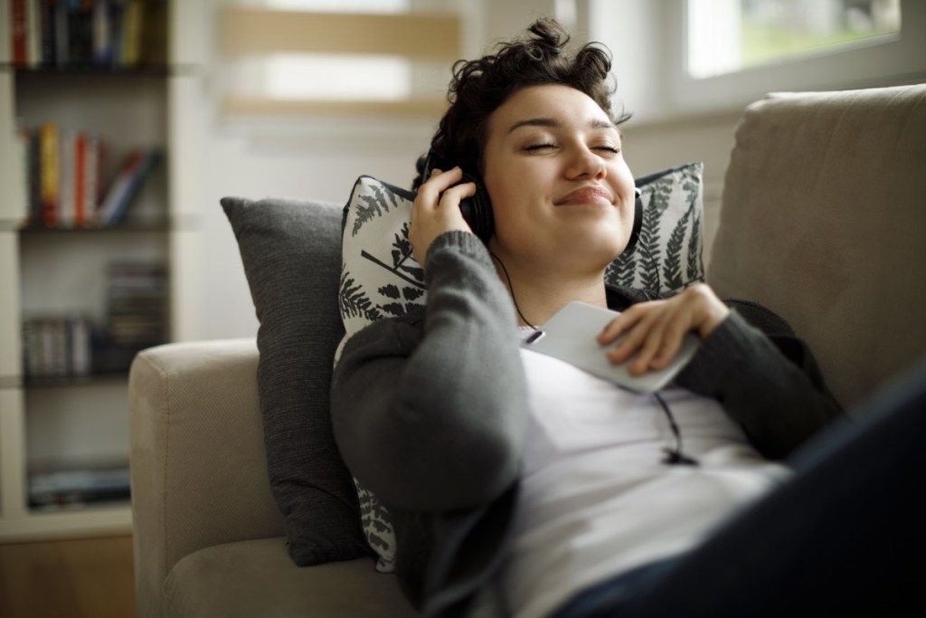 wanita mendengarkan musik baru sambil berbaring di sofa