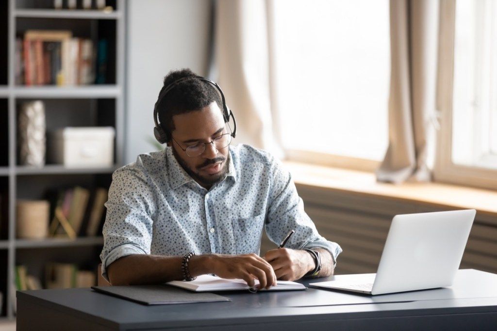 30-vuotias musta mies työskentelee kotitoimistossa kuulokkeilla