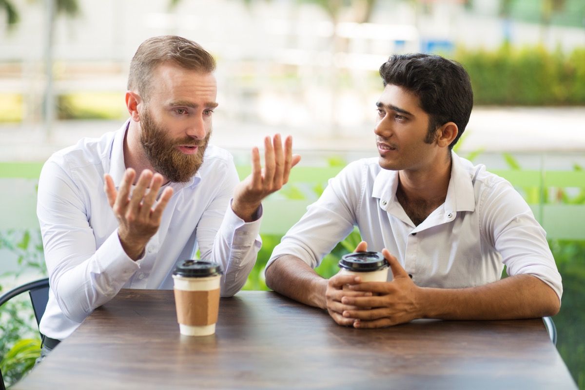 आदमी कॉफी पीते हुए अपने दोस्त से बात करते हुए माफी माँगता है