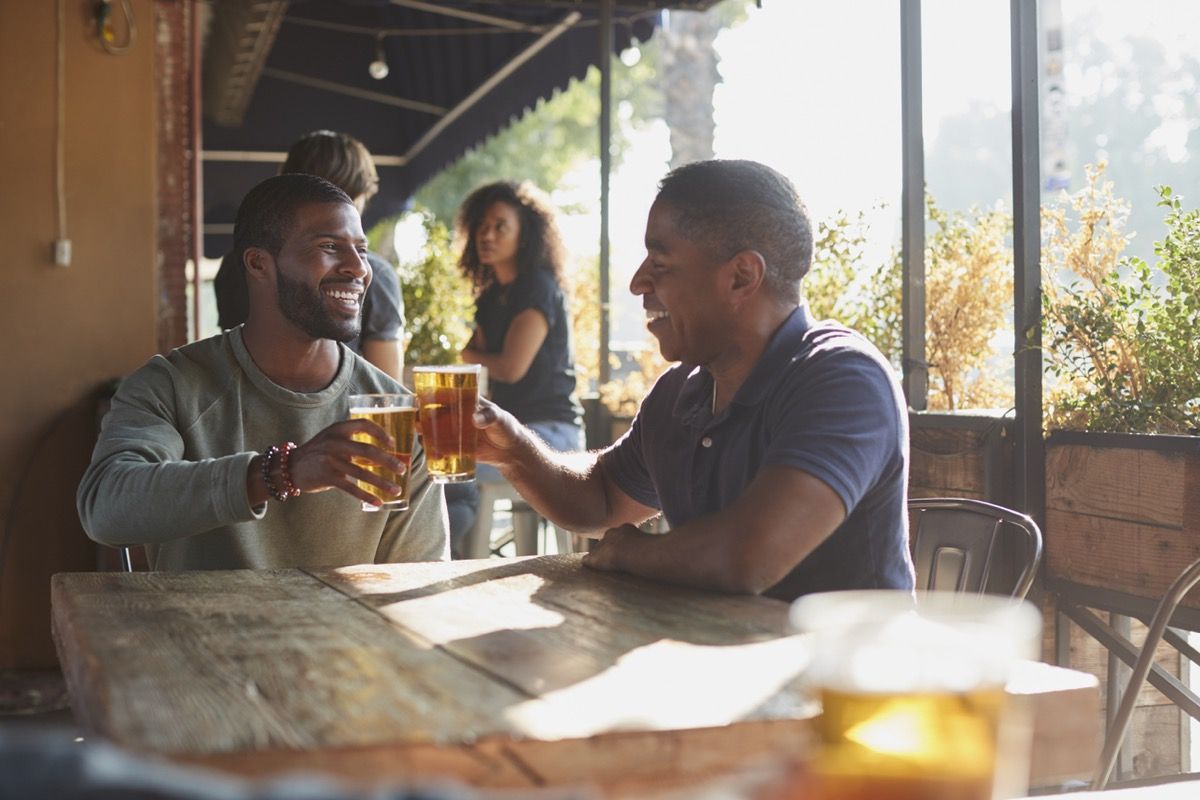 Dos hombre negro de mediana edad brindando cerveza en el patio de un bar deportivo