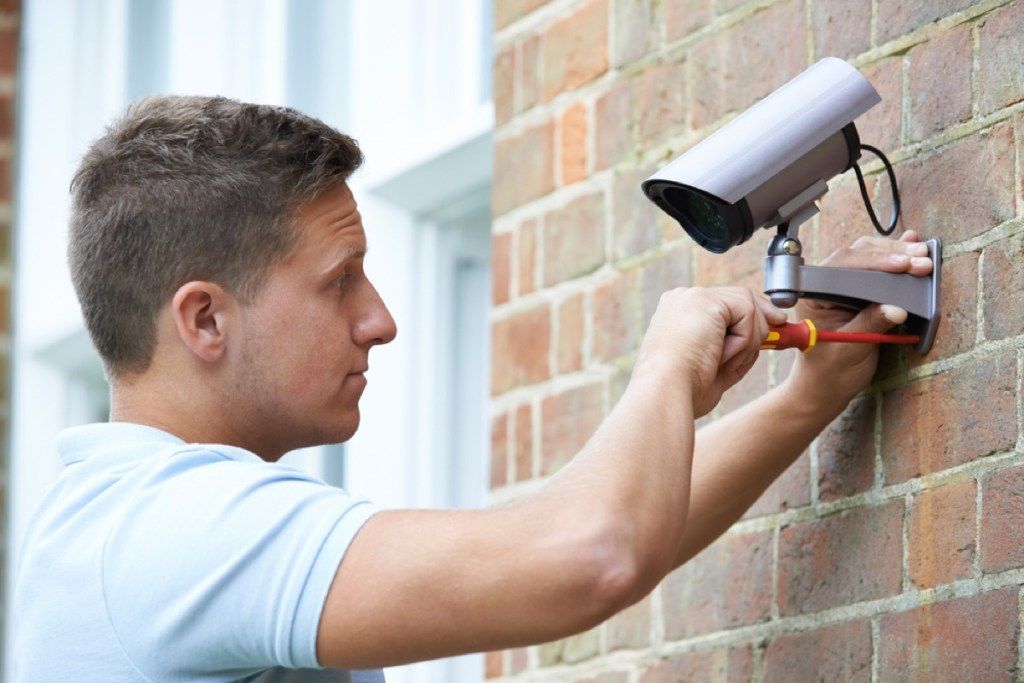 Hombre instalando cámara de seguridad, malas renovaciones en el hogar
