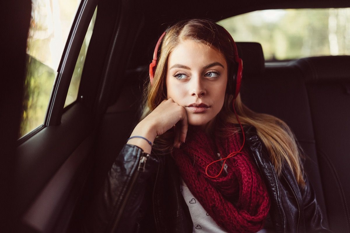 hvit tenåringsjente lei seg i baksetet med hodetelefoner på biltur
