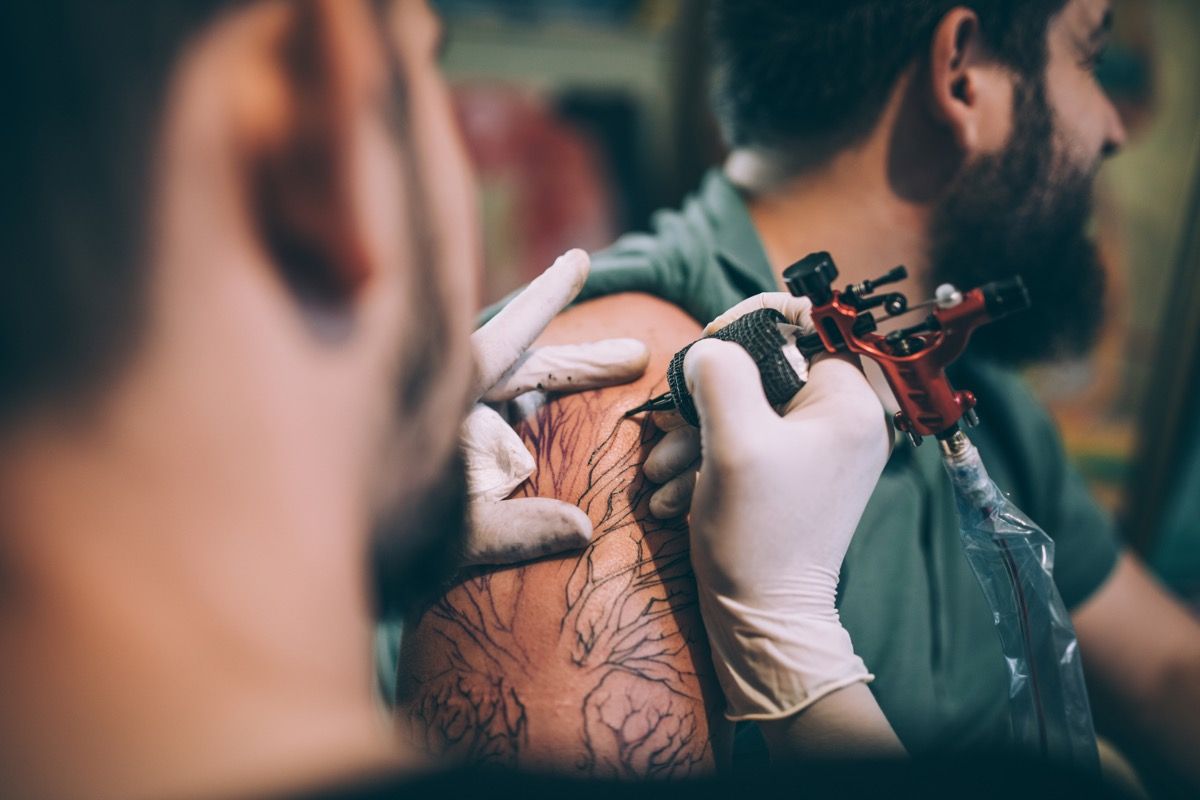 To menn, tatoveringskunstner som tatoverer en mann