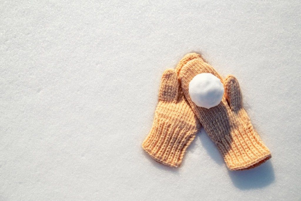 Śnieżka leży na rękawiczkach na czystym białym śniegu w słoneczny mroźny dzień. Widok z góry