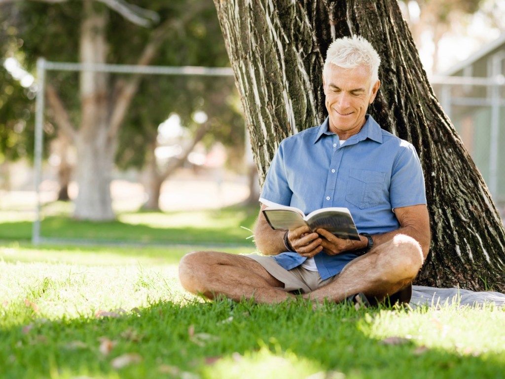 آدمی پارک میں ایک درخت سے پڑھ رہا ہے