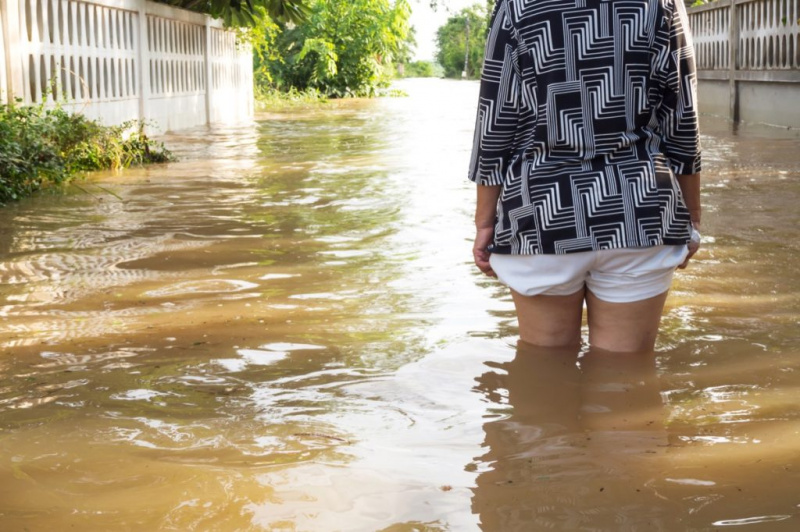  Жена гази наводнение в къщата си. Близък план на крака й. Изглед отзад. Наводнение в провинция Лоей, Тайланд.