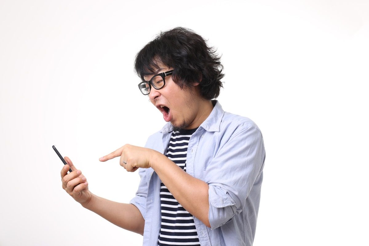 азиатски мъж с очила и дълга коса крещи и сочи към телефона, като не иска да каже на представителя на обслужването на клиенти
