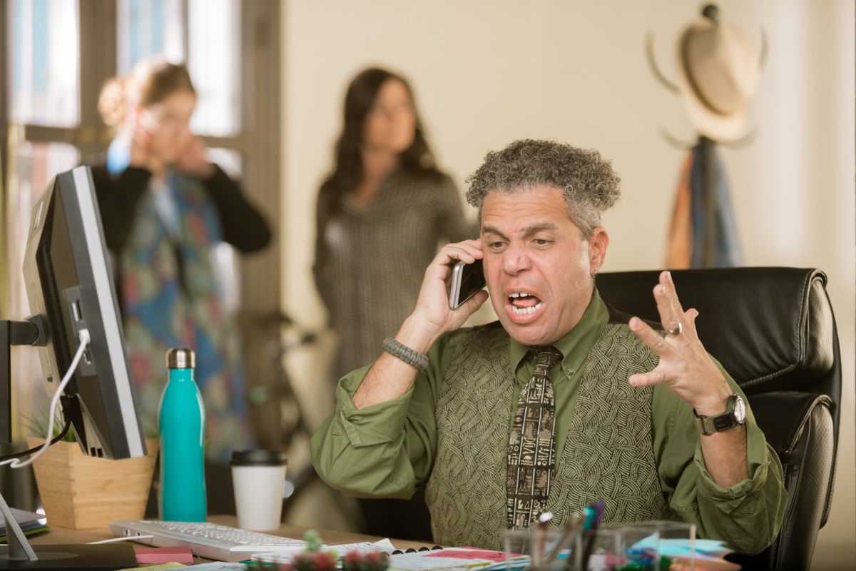 Цветен мъж седи на бюрото и крещи по телефона, като не казва на представителя на обслужването на клиенти