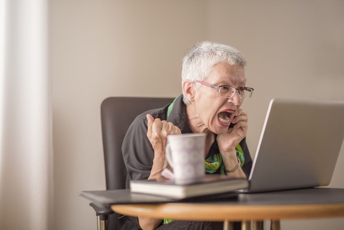 Ældre kvinde med hvidt kort hår og briller skriger mod computeren, mens hun er på telefon, ting ikke at sige til kundeservicemedarbejder