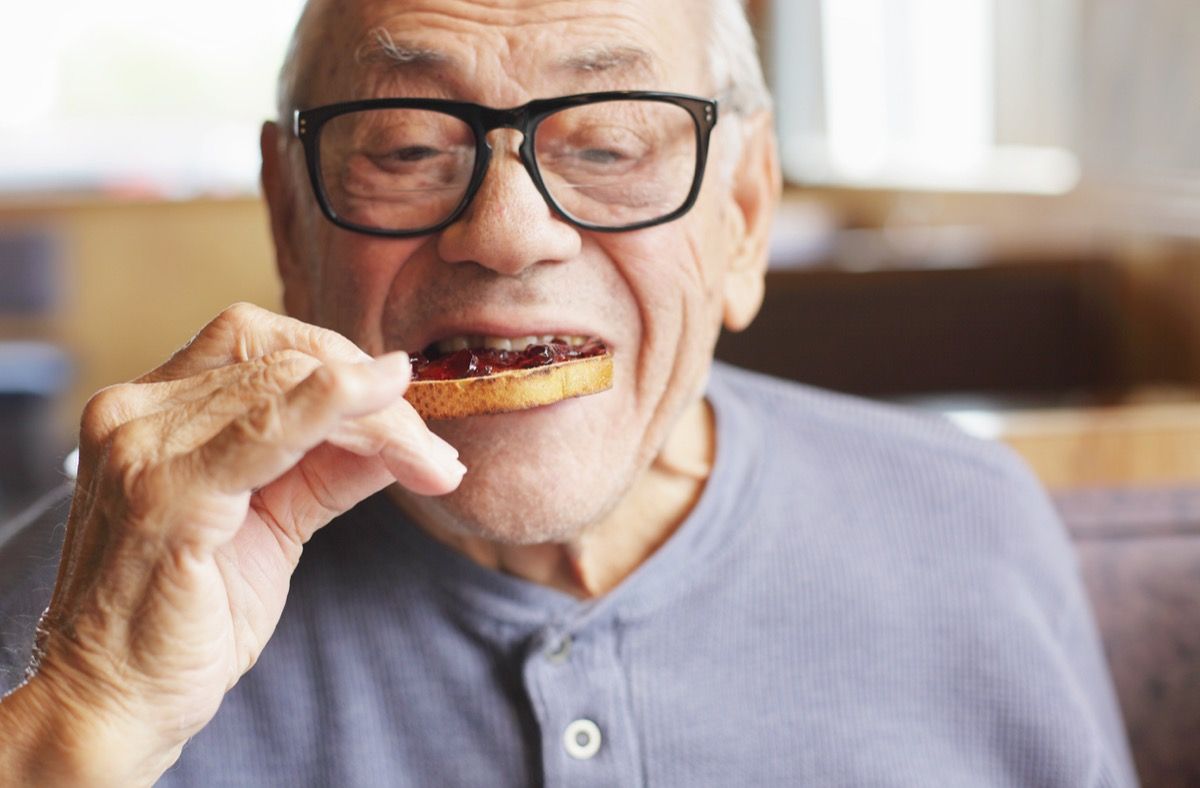 Một người đàn ông cao tuổi thưởng thức miếng bánh mì nướng phết mứt thạch ngọt ngào trong bữa sáng tại nhà hàng.