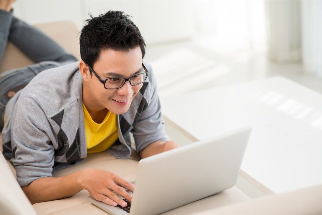 Sretni azijski čovjek radi od kuće na svom laptopu