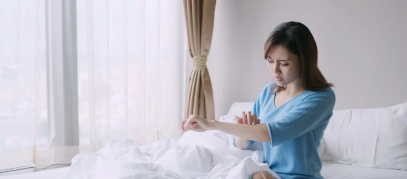   Kvinne klør armen i sengen etter insektbitt