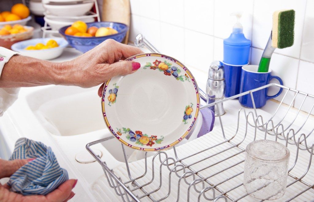 Beschnittenes Bild der älteren Frau, die Platte im Gestell am Küchentisch anordnet