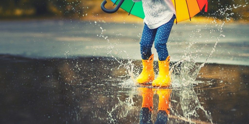 雨の中で水たまりを飛び越える黄色いゴム長靴の子供の足-画像