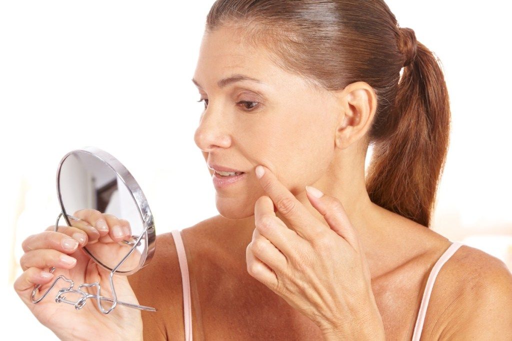 femme tenant un miroir vérifiant sa peau, change de plus de 40