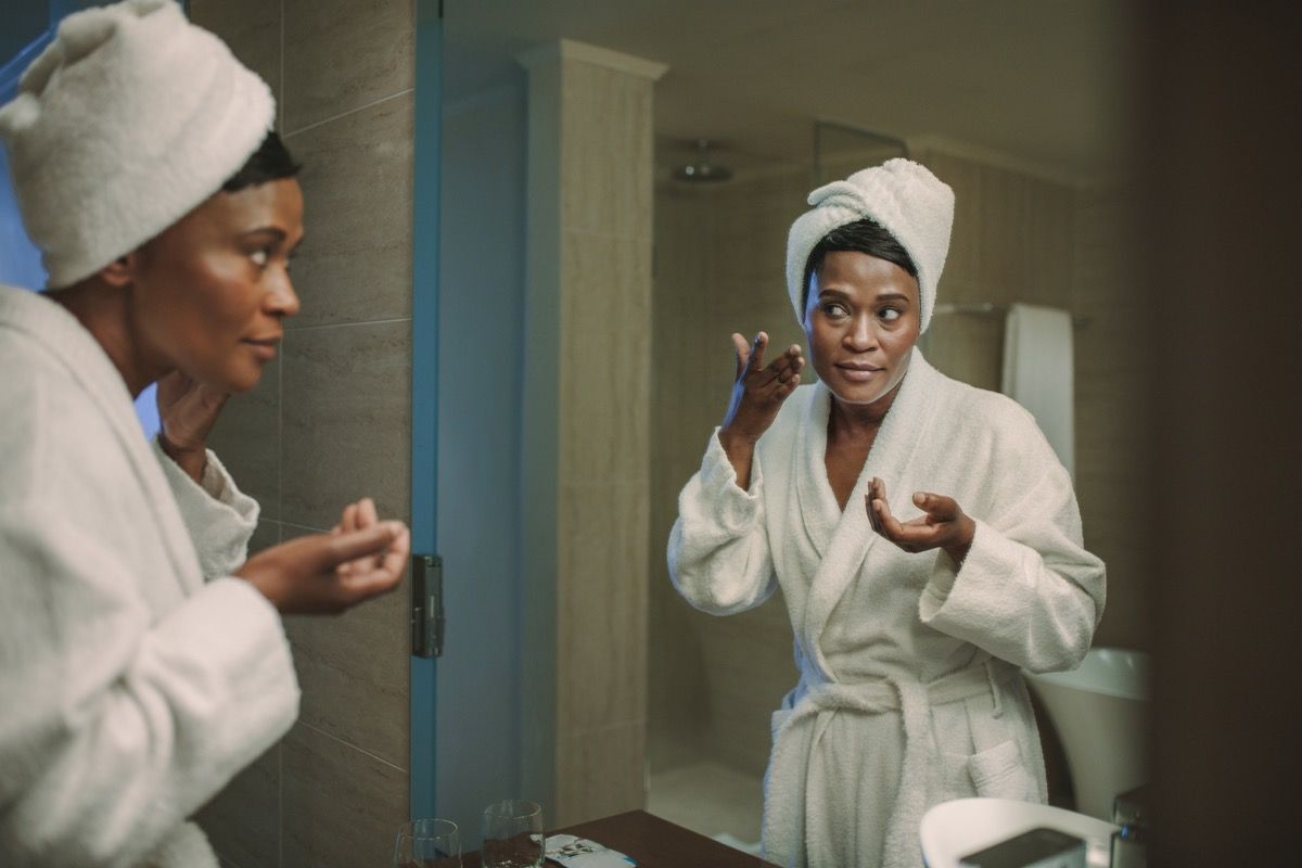 Femme afro-américaine, appliquer la crème pour le visage dans le miroir des symptômes de santé silencieuse