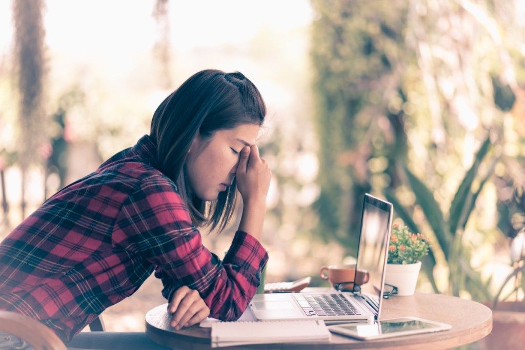 stresset kvinne foran laptop sitter på utendørs kafé