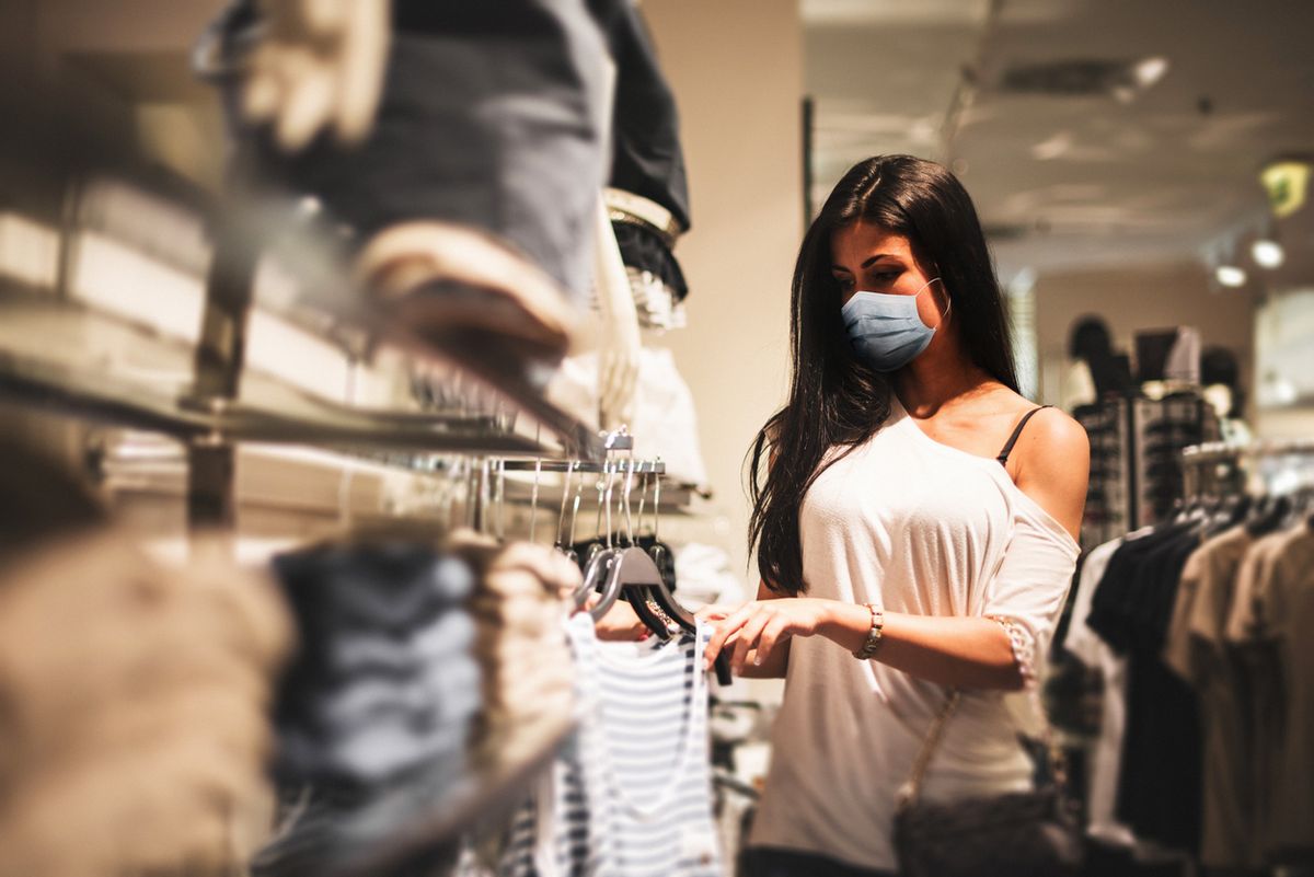 Egy fiatal nő, aki maszkot visel, egy kiskereskedelmi ruházati üzletben vásárol a koronavírus-járvány közepette