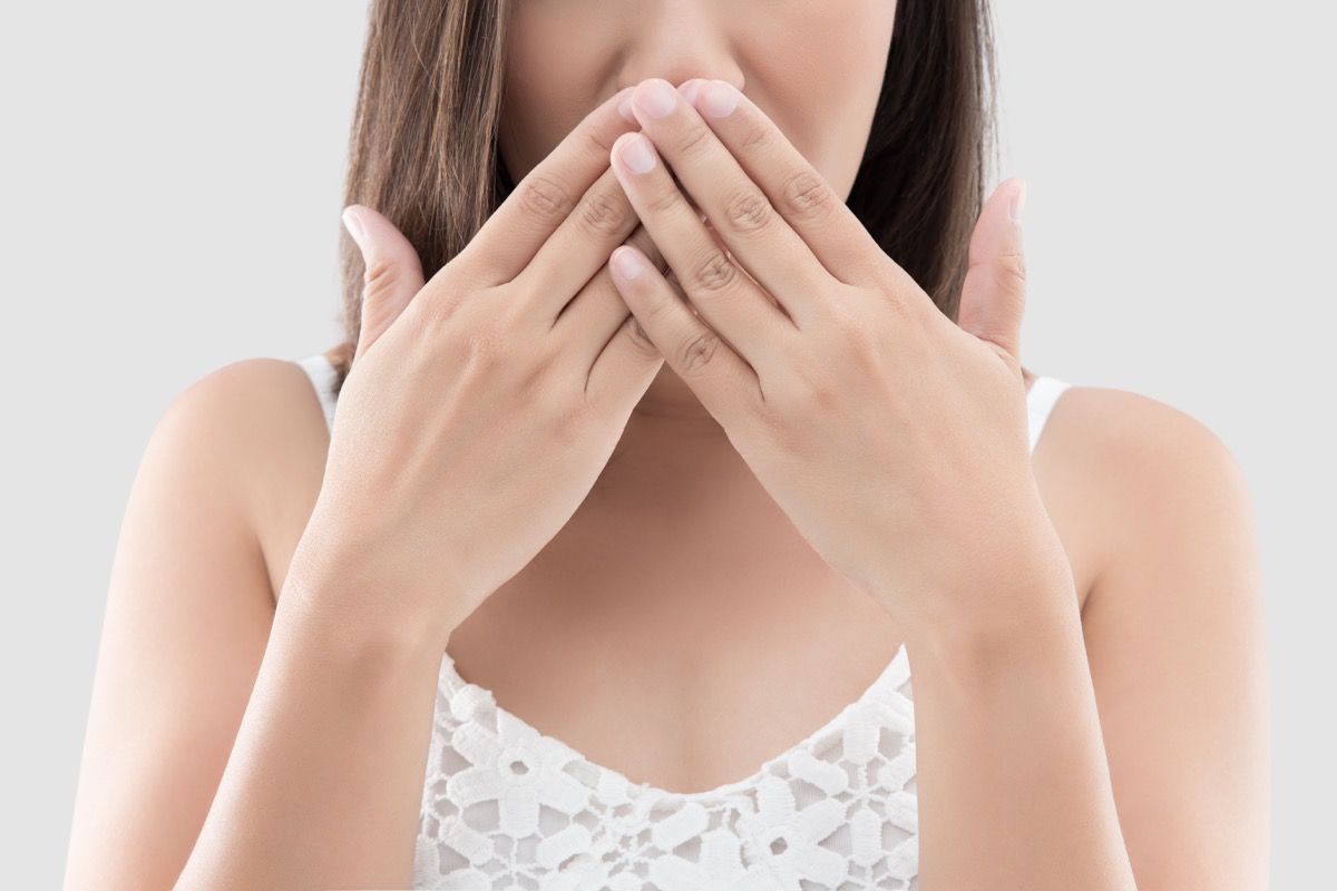 Frau benutzen beide Hände, um den Mund zu schließen, um den grauen Hintergrund nicht zu kommentieren oder abzulehnen