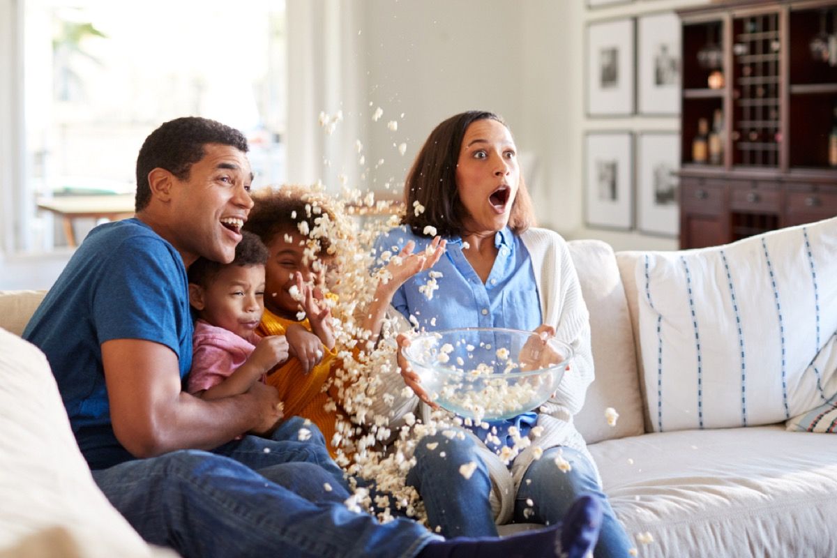 familie pe canapea uitându-se la film în timp ce popcornul se varsă pe podea, cele mai bune filme de Halloween pentru copii