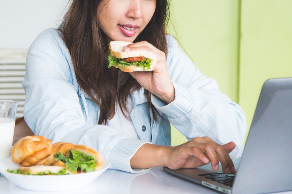 kvinna på jobbet som äter lunch vid sitt skrivbord