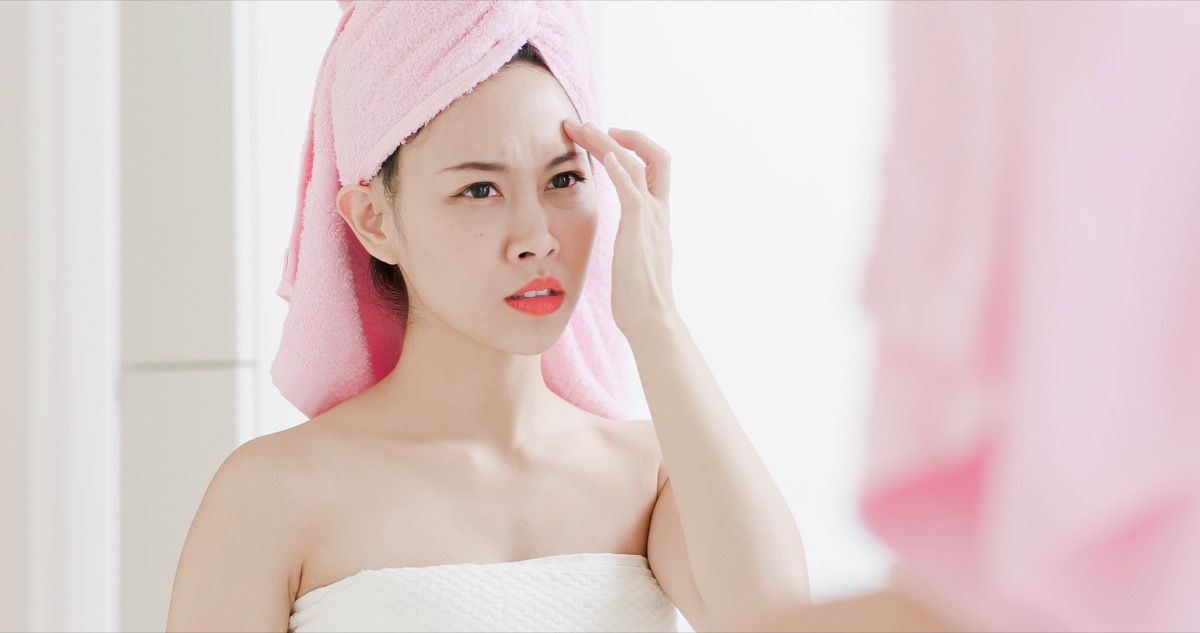 Азиатска жена, гледаща бръчките и петна по лицето си в огледалото