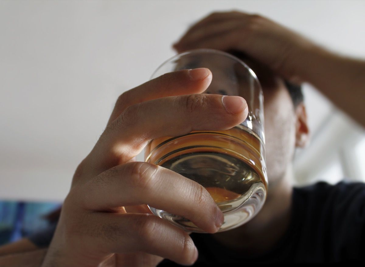 Млад мъж, държещ чаша алкохол с ръка на главата, прострелян отдолу под стъклото в лицето му