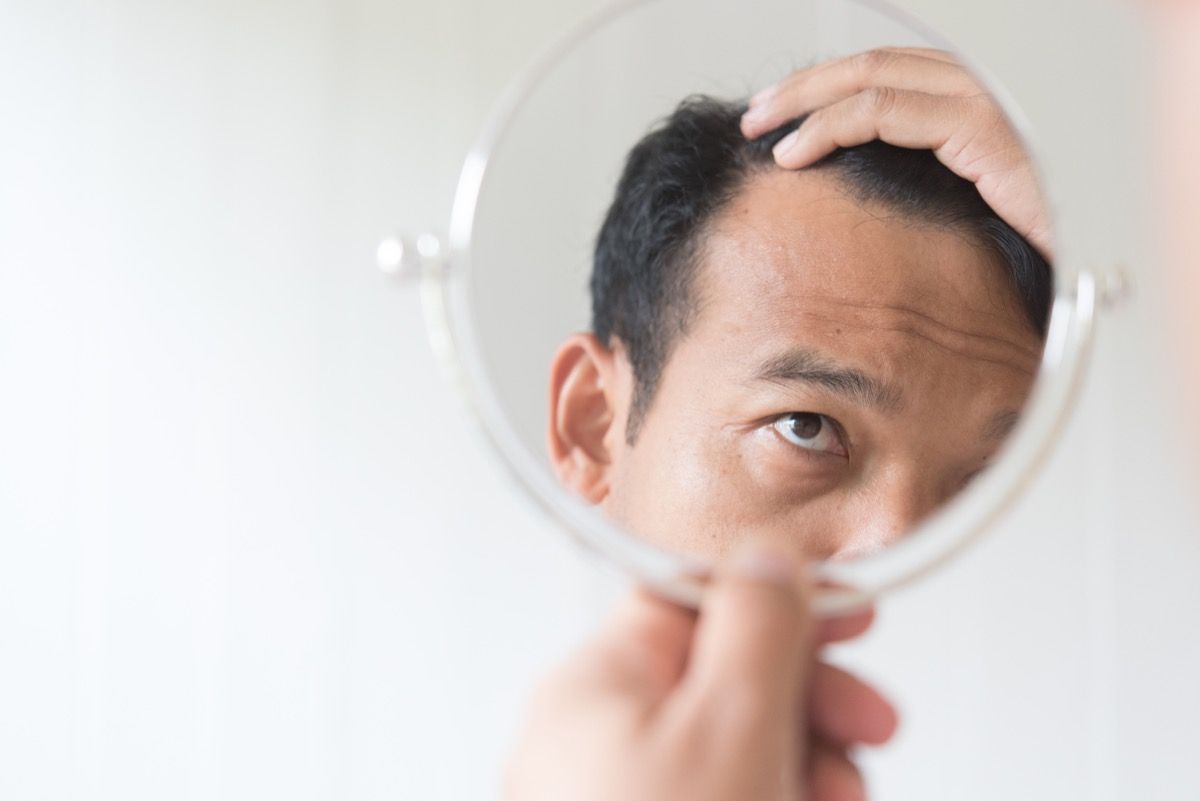 vecāks vīrietis skatās spogulī uz matu izkrišanu, vairāk nekā 50 nožēlo