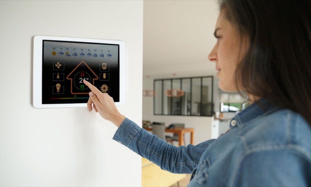 Sieviete, izmantojot savās mājās viedo tehnoloģiju termostatu