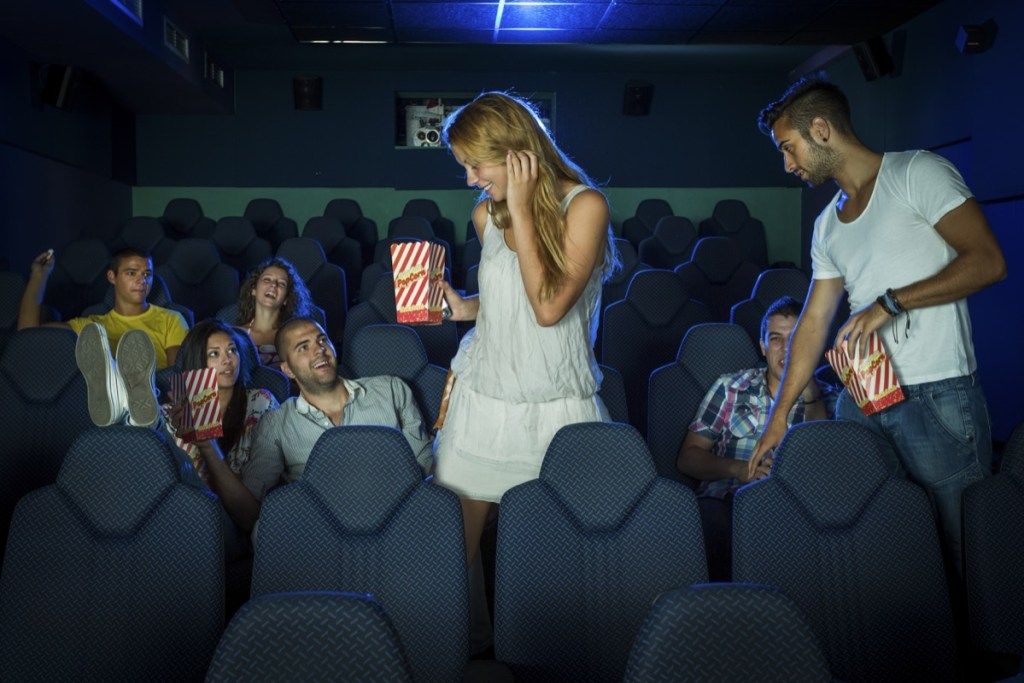 một người đàn ông và một người phụ nữ cầm bỏng ngô đi qua những người đang ngồi để về chỗ của họ xem phim
