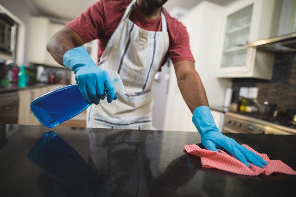 Keskiosa mies puhdistaa mustaa marmoria tiskillä keittiössä kotona