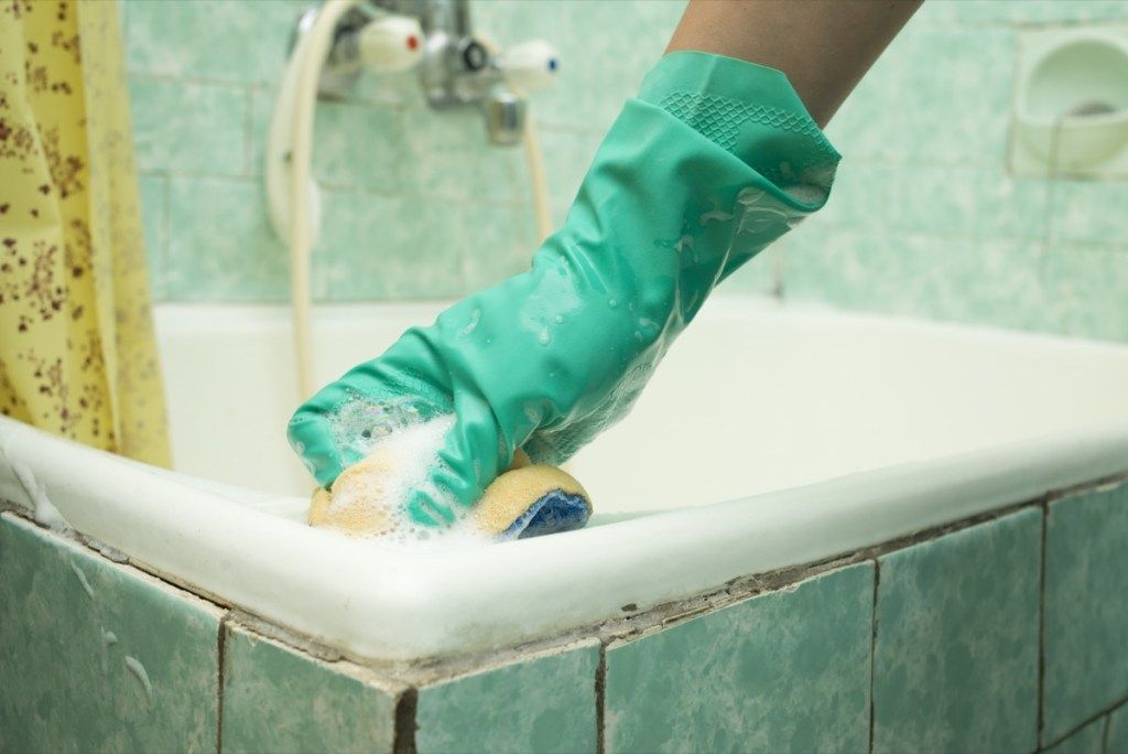 tangan dengan sarung tangan hijau membersihkan bak mandi kotor
