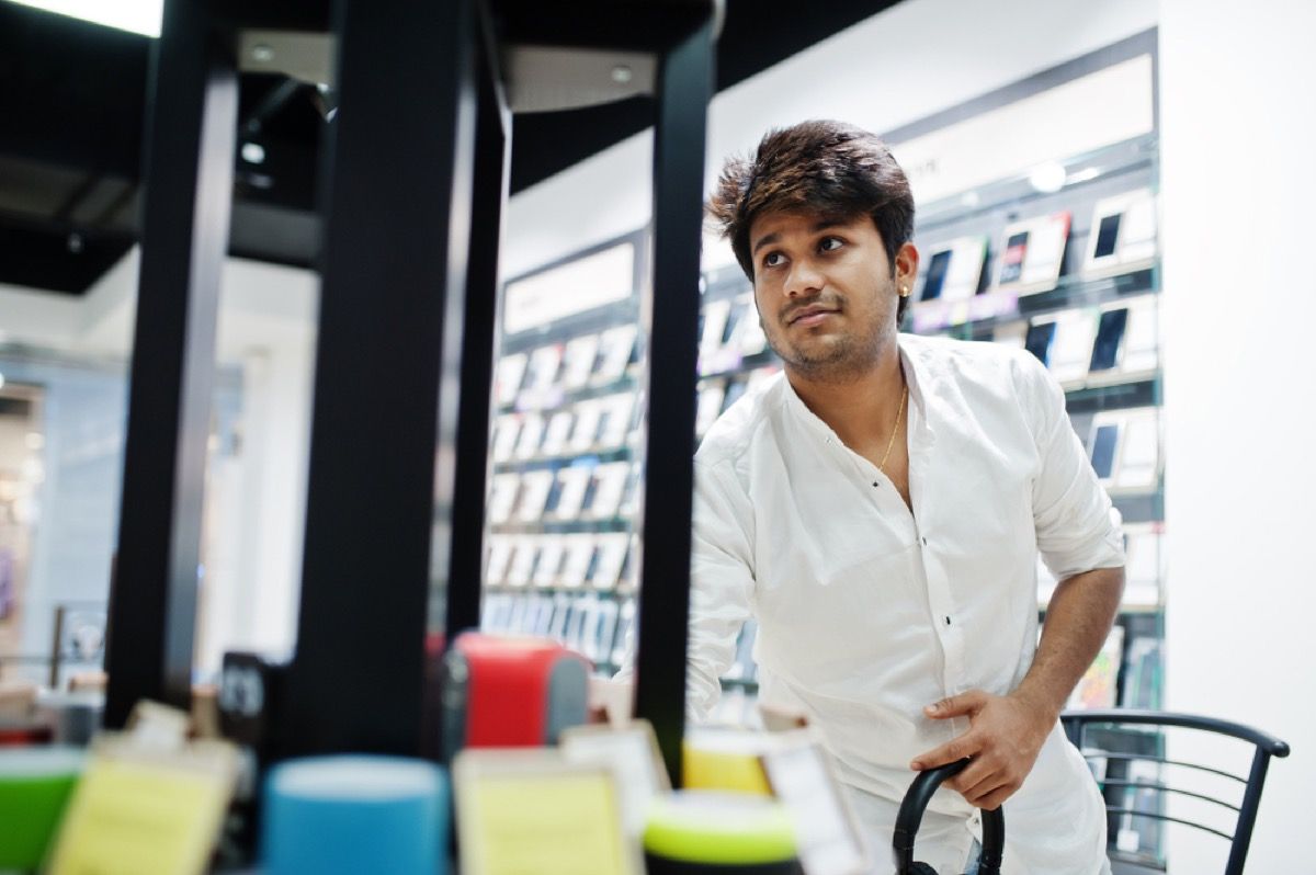 Indijos vyras žiūri į telefoną elektroninėje parduotuvėje