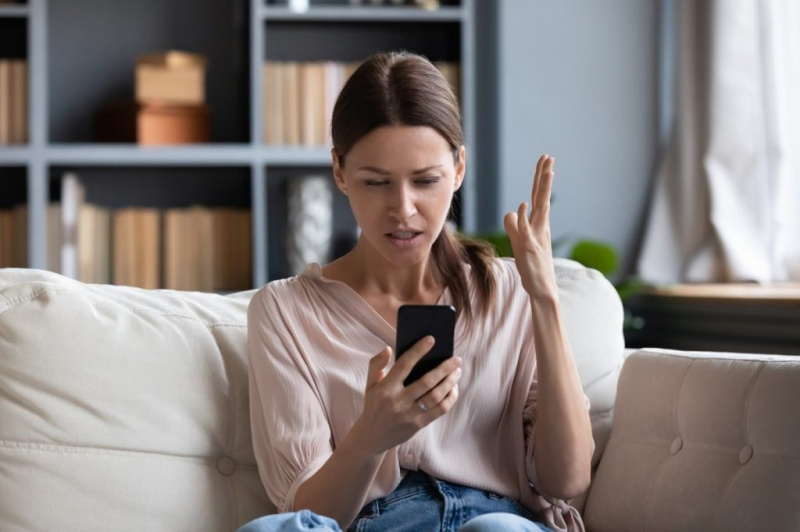   भ्रमित नाराज महिला को फोन की समस्या, घर में सोफे पर बैठी, दुखी युवती स्क्रीन पर देख रही है, डिस्चार्ज या टूटे हुए स्मार्टफोन से असंतुष्ट, मैसेज में पढ़ रही बुरी खबर