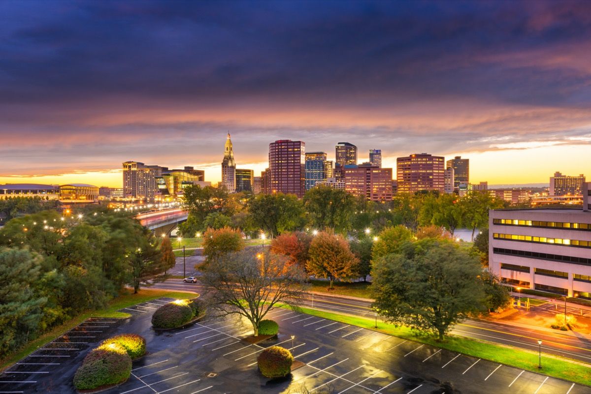 miesto panorama - tuščia automobilių stovėjimo aikštelė, medžiai, pastatai ir judri magistralė saulėlydžio metu Hartforde, Konektikute