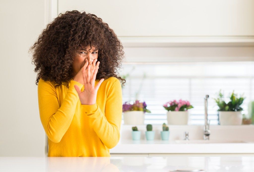 Afroamerikanka koja u kuhinji nosi žuti džemper u mirisu nečeg smrdljivog i drži se za nos