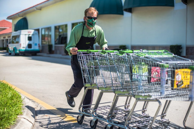  „Publix“ bakalėjos parduotuvės darbuotojas su veido kauke grąžina vežimėlius į parduotuvę iš automobilių stovėjimo aikštelės