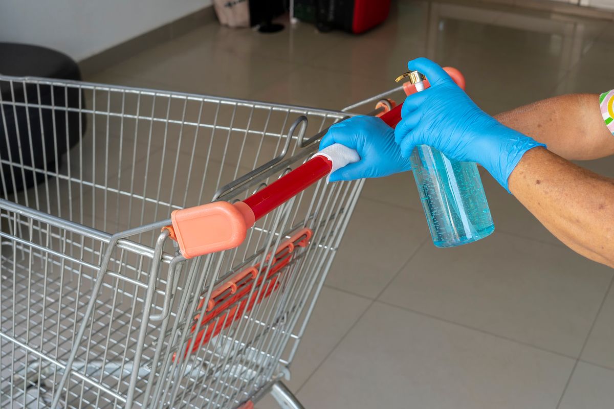 Naiste töötajad desinfitseerivad ostukorvi, piserdades pudelist niiskele salvrätile sinist puhastusvahendit.