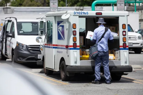   Un camion poștal USPS (United States Parcel Service) și un transportator poștal efectuează o livrare.